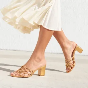 Gold woven sandals worn with an ivory dress in sunlight